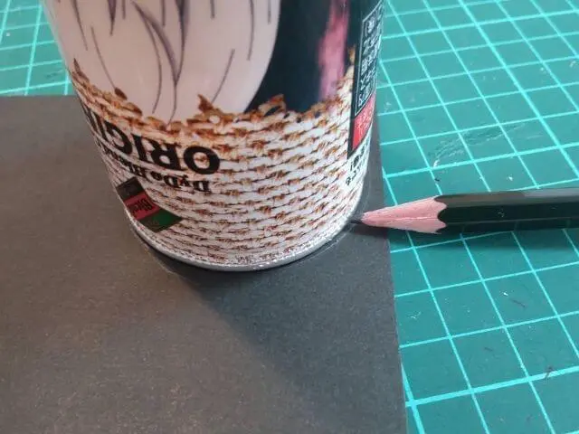 黒色の厚紙に呪術缶を置いて鉛筆でなぞって丸形を作っている写真