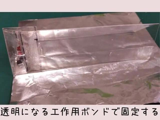 プラバンで作った正三角形の筒をアルミホイルの輝いている方で包み込み、透明になる工作用ボンドとセロハンテープで固定する写真